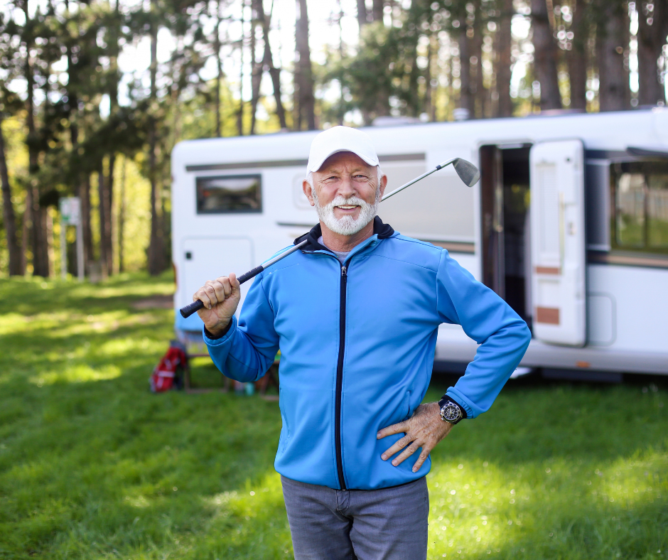 Retired Australian grey nomad man standing in front of caravan at forest campsite with golf club — caravan finance retirement lifestyle